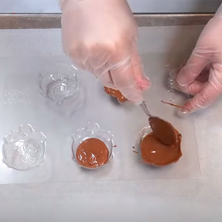 filling a turtle shaped chocolate mold with melted chocolate and spreading with spoon
