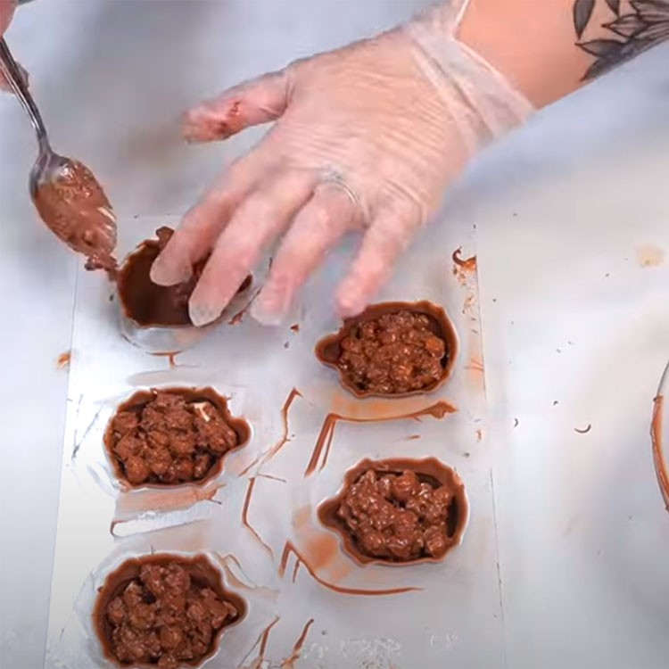 melted chocolate, caramel, and pecan mixture being spoons into turtle shells
