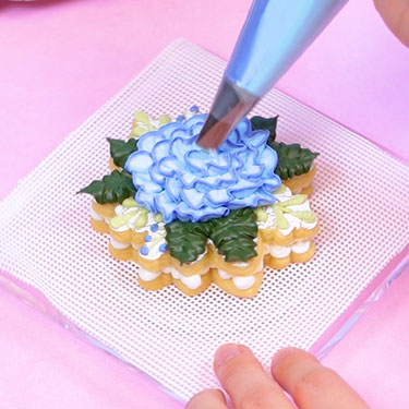 using a rose tip to pipe a buttercream flower onto a sugar cookie