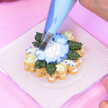 piping a buttercream flower onto cookie