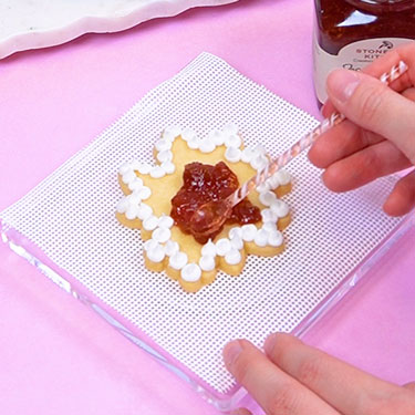 spreading jam onto baked sugar cookie