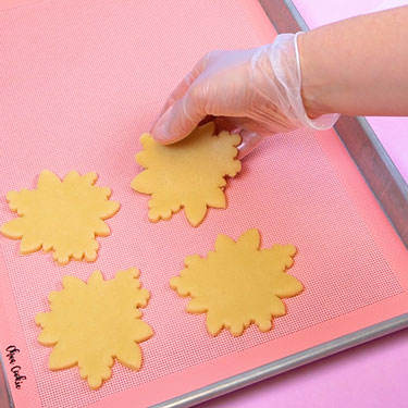placing cut out cookies onto a baking sheet lined with a chua mat