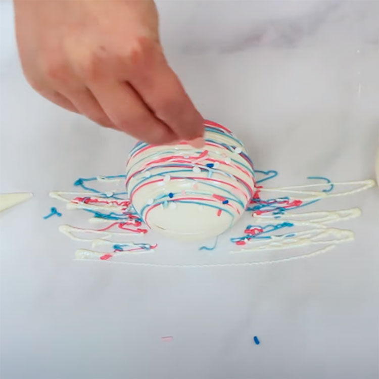 adding blue and pink sprinkles to a gender reveal hot cocoa bomb