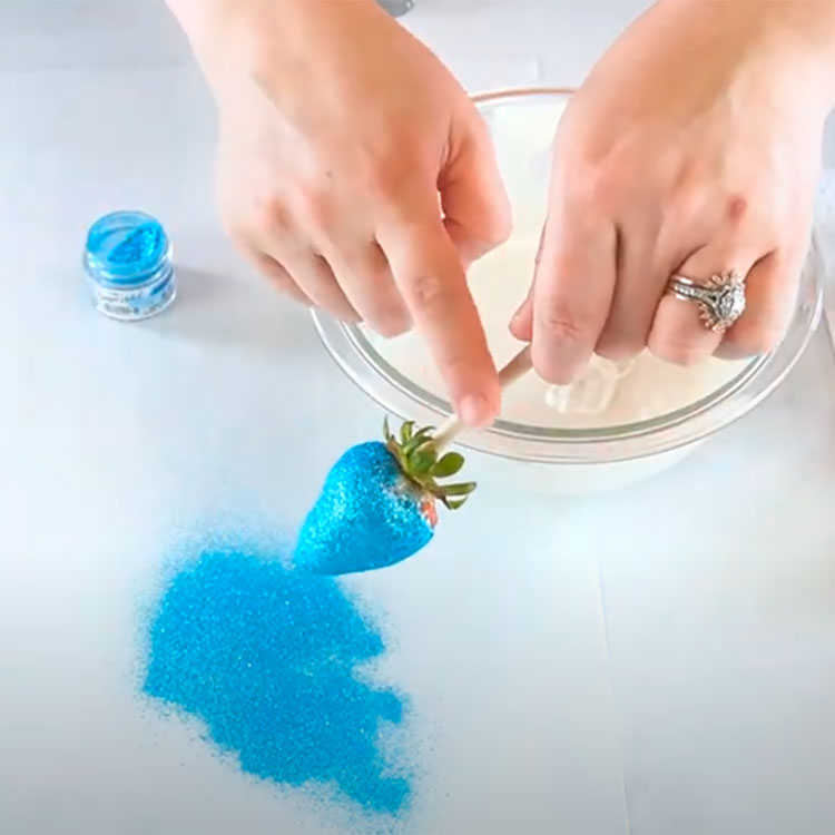 sprinkling edible blue glitter onto a chocolate coated strawberry