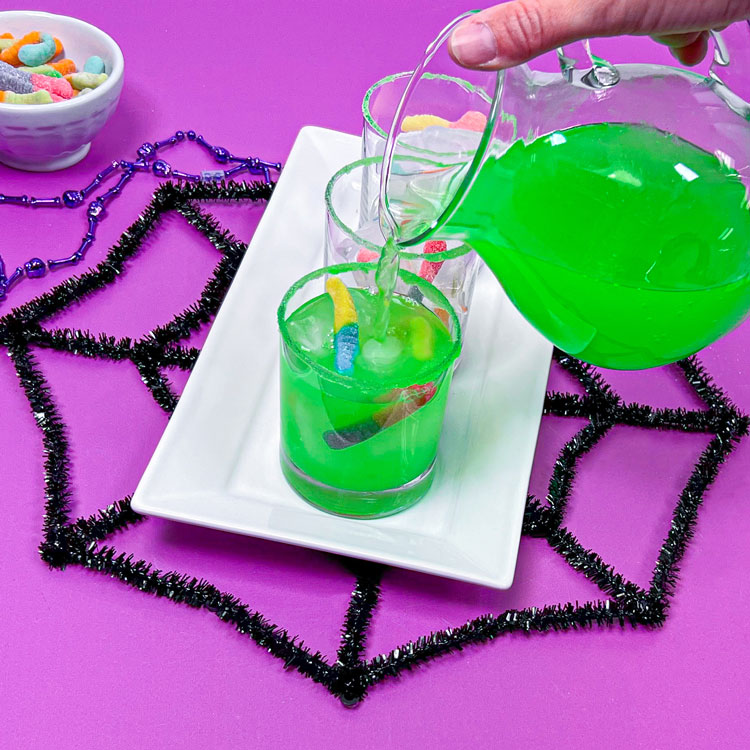 pouring green drink into glasses filled with ice and gummy worms