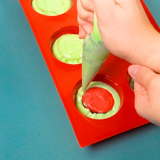 piping melted green chocolate on top of oreos in mold