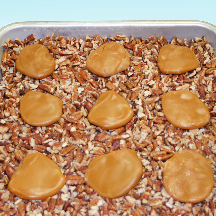 pan with a layer of pecan pieces with mounds of caramel on top