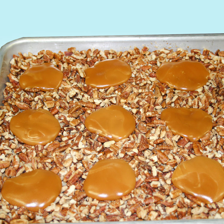 pan with a layer of pecan pieces with mounds of melted caramel on top