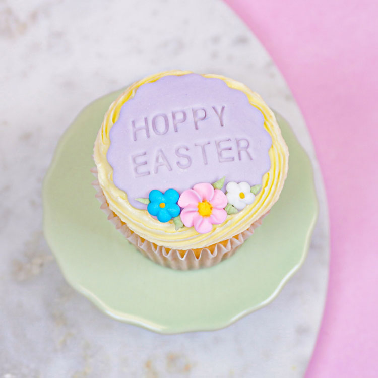 yellow frosted cupcake with a purple fondant plaque that says hoppy easter