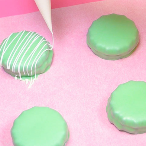 drizzling melted white chocolate onto chocolate covered sandwich cookie