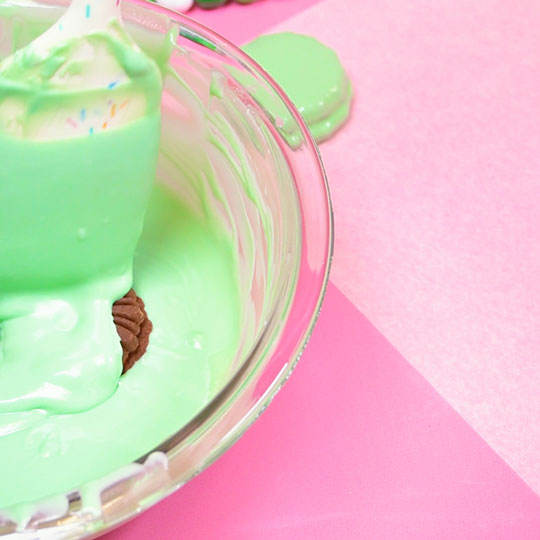 spooning melted green chocolate over chocolate sandwich cookie