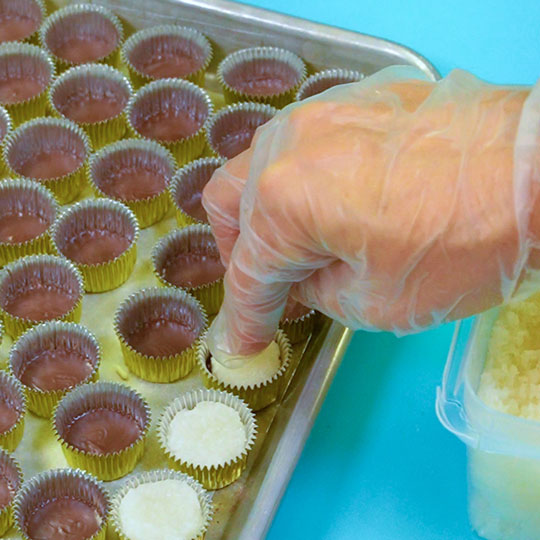 pressing coconut dough into candy cup filled with dark chocolate