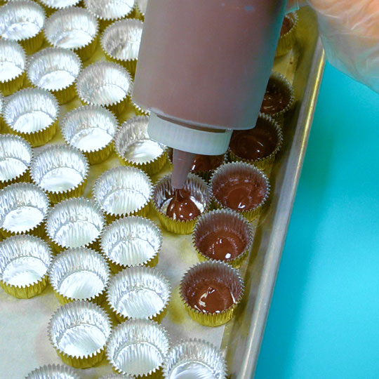 filling foil candy cups with melted dark chocolate using squeeze bottle