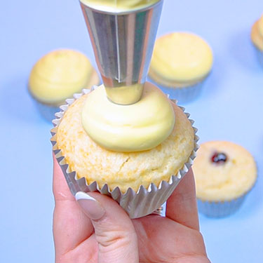 using a piping bag fitted with a round tip to frost a cupcake
