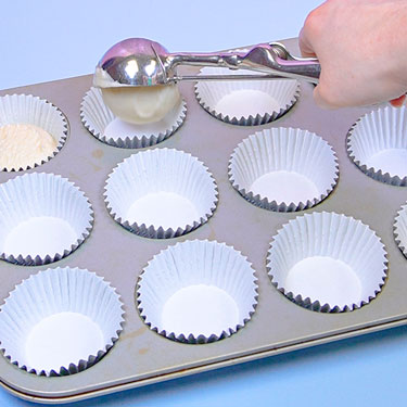 scooping vanilla cake batter into cupcake pans