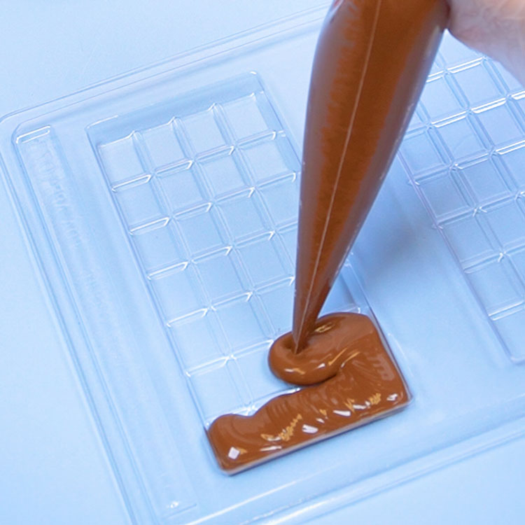piping melted milk chocolate into candy bar chocolate mold