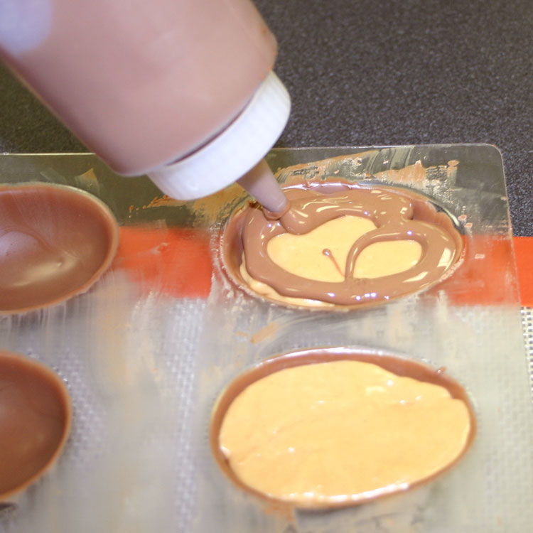 adding chocolate on top of peanut butter candy center to seal the eggs