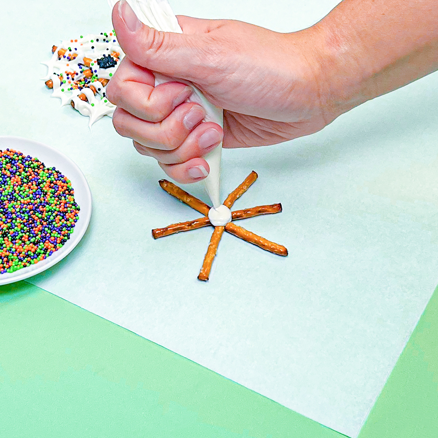 piping white chocolate into center of pretzel spider web