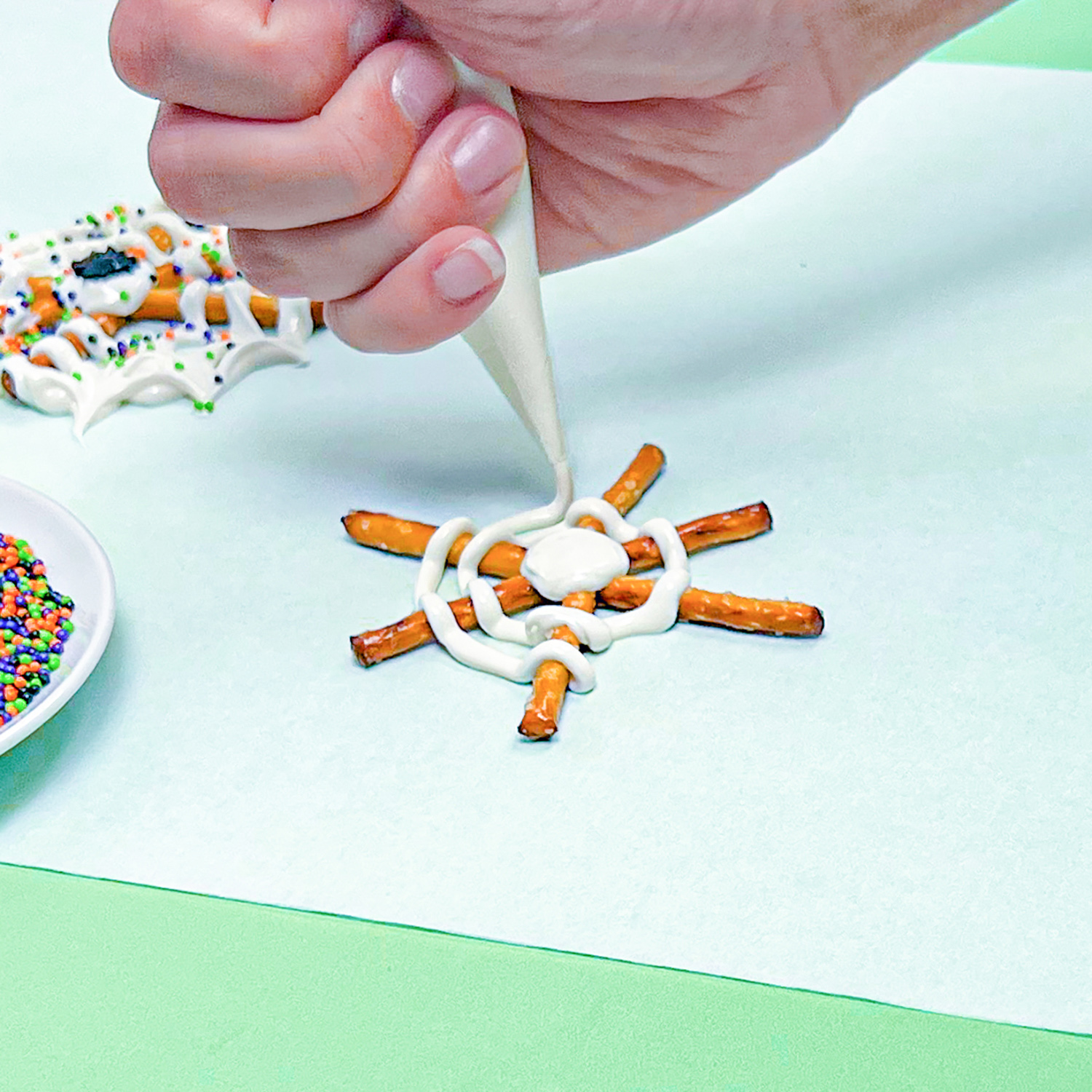 piping rings of white chocolate onto pretzel spider web