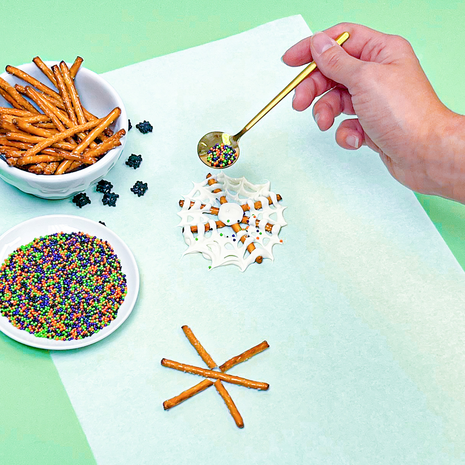 adding sprinkle mix with sprinkle spoon onto chocolate spider web