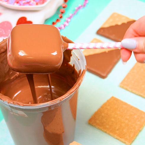 tapping excess chocolate off of marshmallow