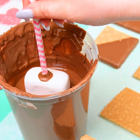 dipping marshmallow into melted milk chocolate