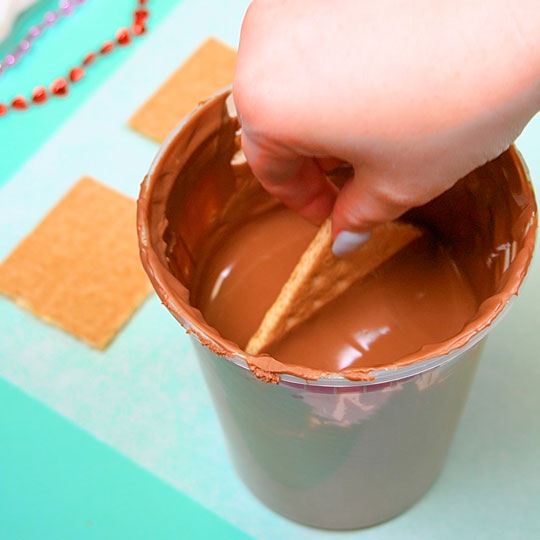 dipping graham cracker into melted milk chocolate