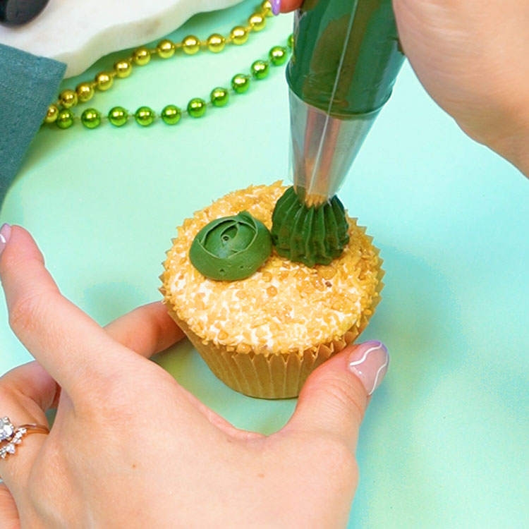 piping buttercream cactus onto cupcake