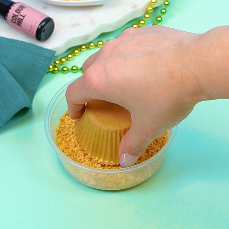 dipping frosted cupcake into coconut crunch