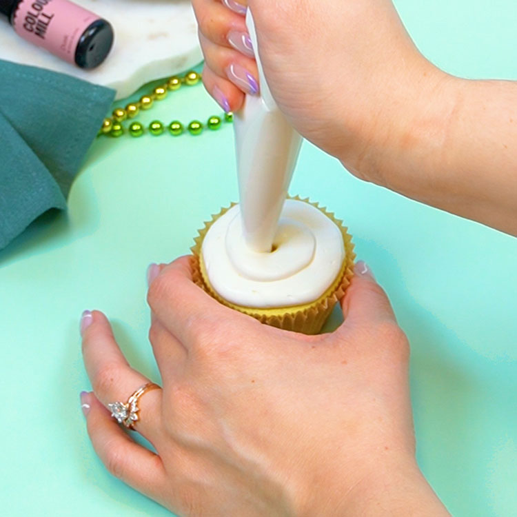 piping white buttercream onto a vanilla cupcake