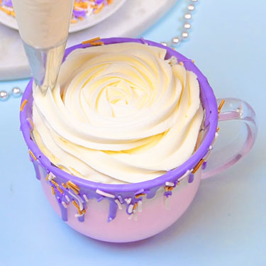 piping whipped cream into mug filled with hot chocolate