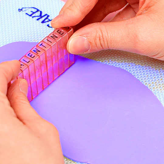 pressing letter embossers into purple fondant